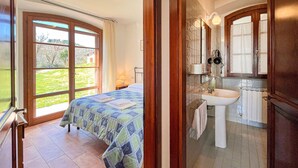 A bedroom with a large window, a bed with a quilt, and a bathroom with a sink and mirror. - Amazing apartment in Gubbio with WiFi (Gubbio)