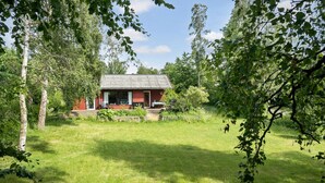 A red wooden cabin with a tiled roof, surrounded by lush greenery and trees. - Awesome home in Jægerspris with WiFi (Jægerspris)