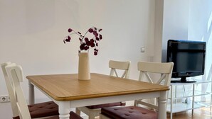 Zona pranzo con tavolo in legno, sedie bianche e un vaso con fiori.