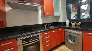 Una cucina con mobili rossi, un piano di lavoro nero, un fornello, un lavello e una lavatrice.