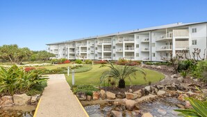 Un hotel de varios pisos con balcones, un jardín ajardinado y un camino que lleva a la entrada.