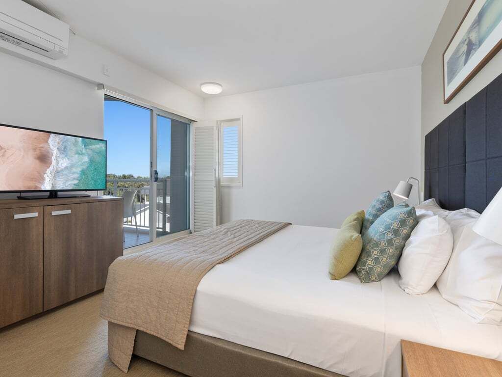 A bedroom with a bed, a TV, a balcony, and a window.