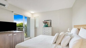 Een slaapkamer met een bed, een televisie, een dressoir, een spiegel en een balkon.