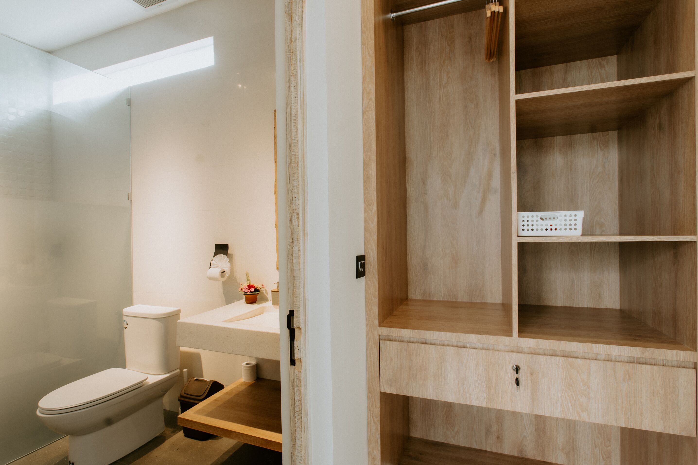 A modern bathroom with a toilet, sink, and wooden shelving unit.