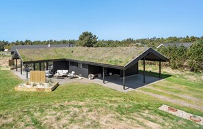 Une maison moderne avec un toit plat, un patio couvert et une cour gazonnée.