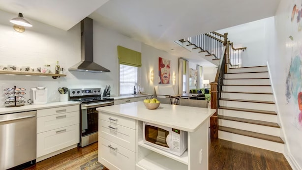 A modern kitchen with white cabinetry, a built-in oven, and a microwave. There is a wooden staircase leading to another level.
