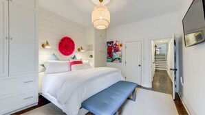 A bedroom with a large bed, a bench, a wardrobe, and a door leading to a staircase.