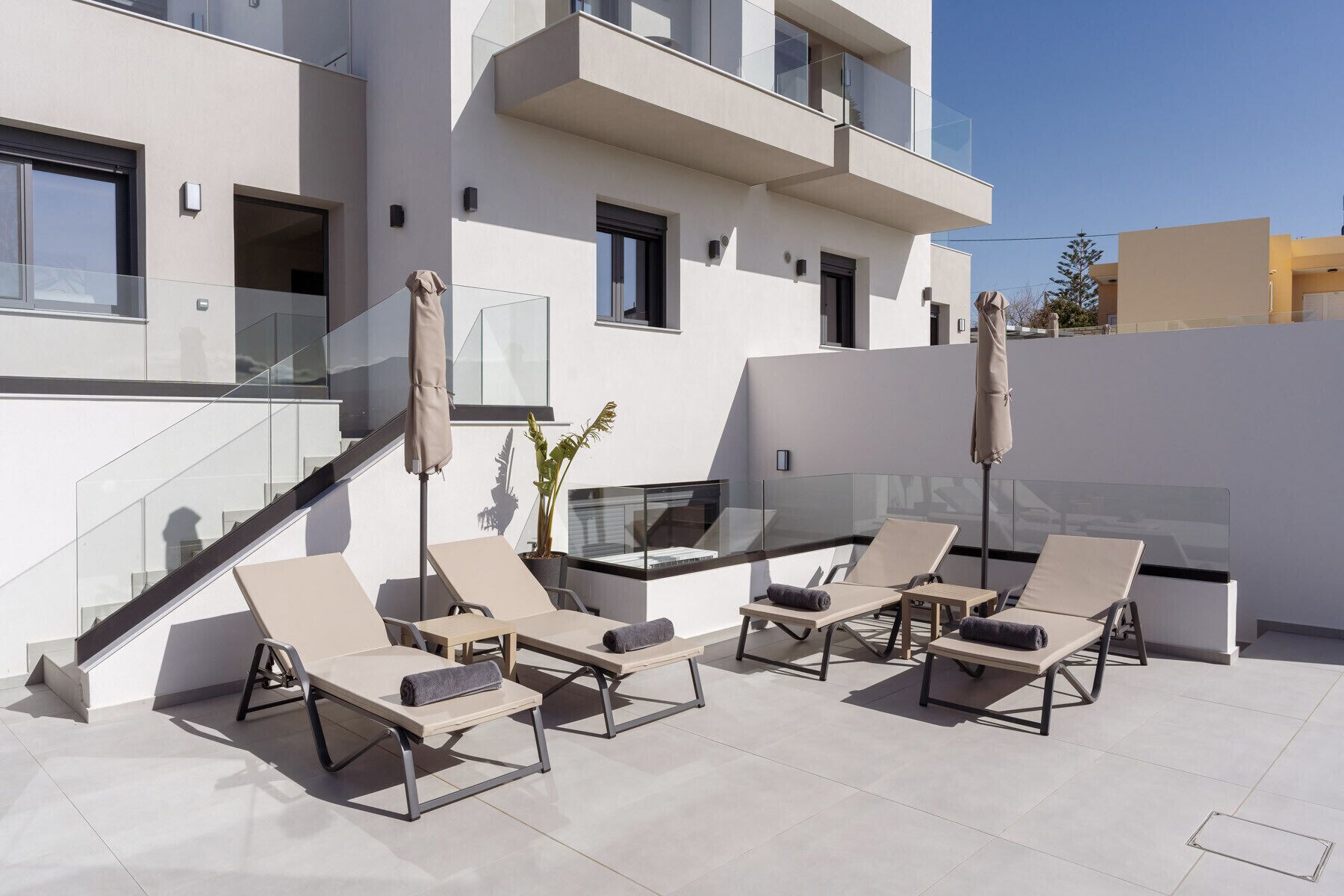 A rooftop terrace with sun loungers, a small table, and a potted plant.