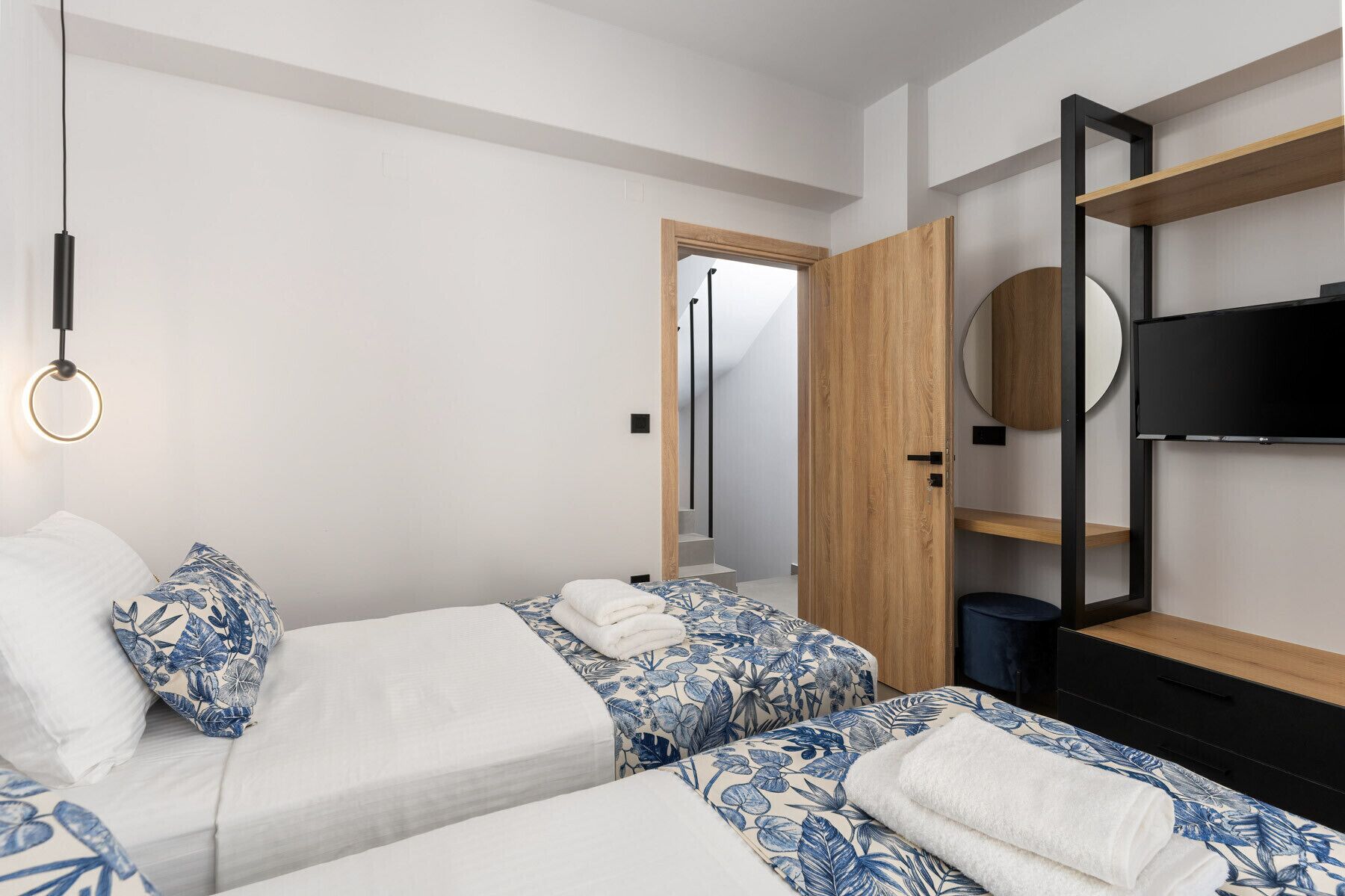 A modern hotel room with two beds, a TV, a mirror, and a ring light.