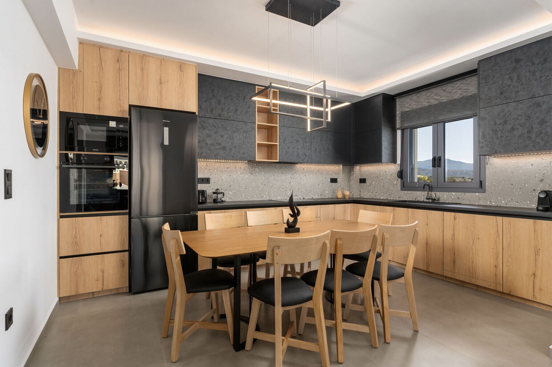 A modern kitchen with wooden cabinets, a black refrigerator, a dining table with chairs, and a window with a view.
