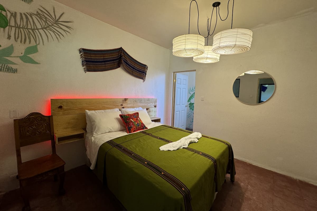 Une chambre à coucher comprenant un lit, une table de chevet, un miroir et un luminaire suspendu.