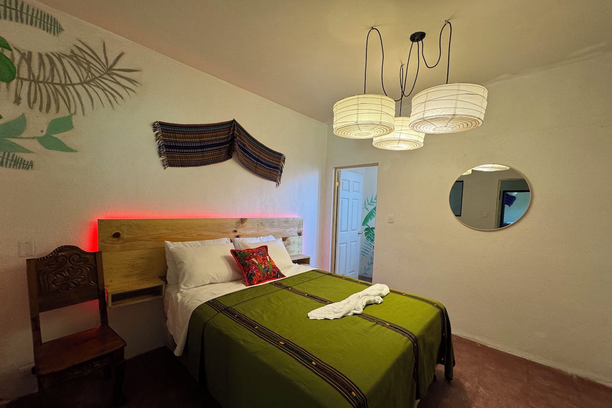 Un dormitorio con cama, mesita de noche, espejo y lámpara colgante.