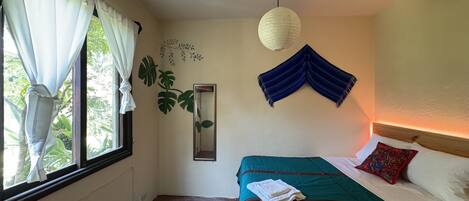 Un dormitorio con cama, ventana con cortinas, lámpara colgante y planta en la pared.