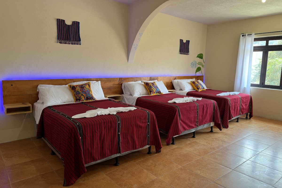 Une chambre d’hôtel avec trois lits, chacun étant doté de draps à rayures rouges et d’oreillers blancs.