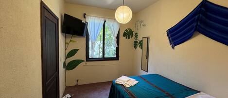 Un dormitorio con una cama, un televisor montado en la pared, una ventana con cortinas y una planta.