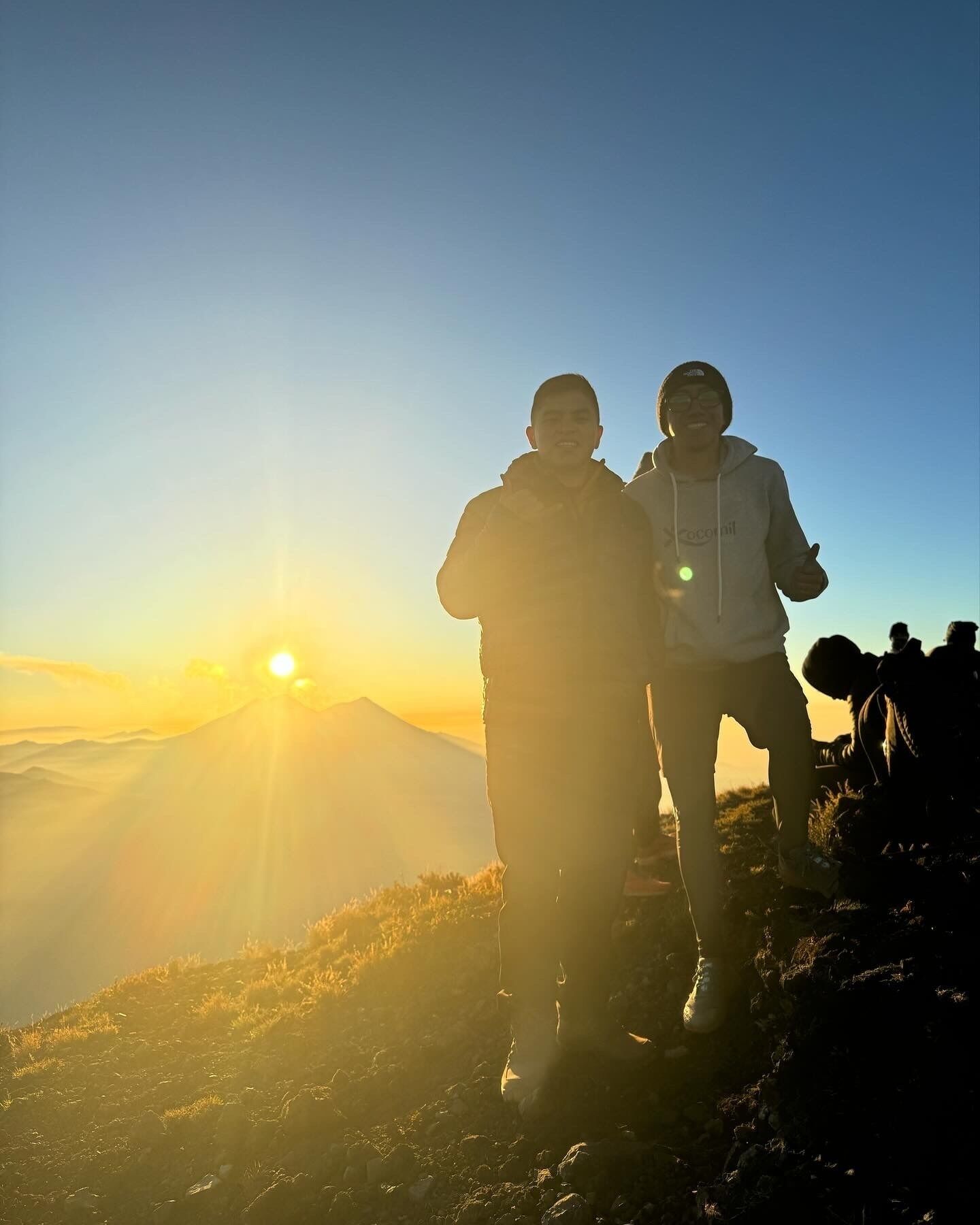 Deux personnes se tiennent sur une montagne, avec un coucher de soleil en arrière-plan.
