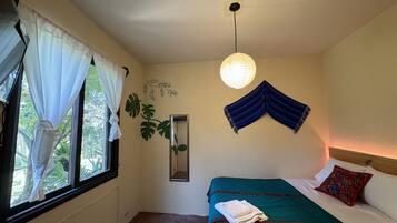 Un dormitorio con cama, una ventana con cortinas, un espejo instalado en la pared y una lámpara colgante.