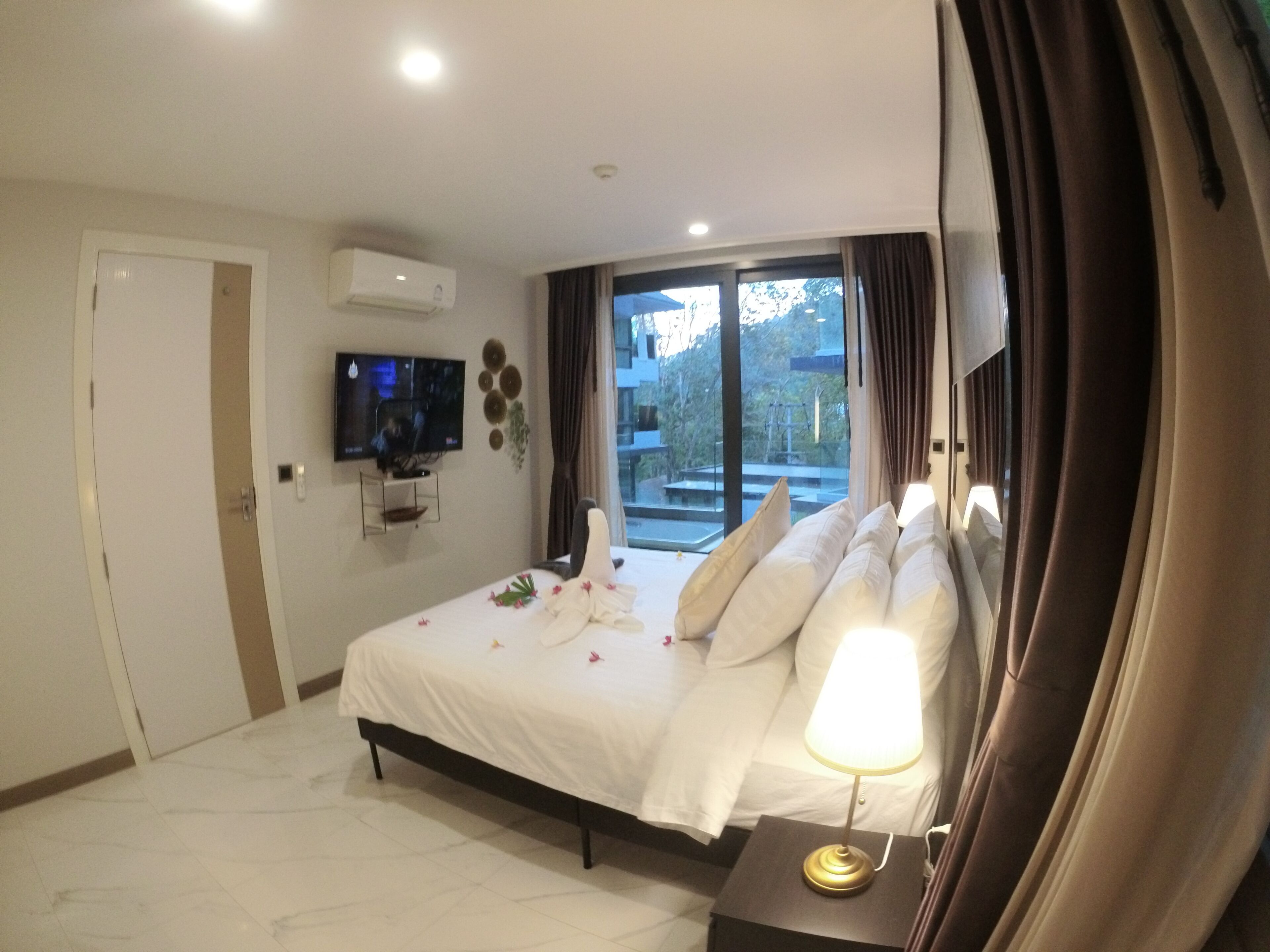A hotel room with a bed, a TV mounted on the wall, a window with curtains, and a view of the outside.