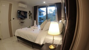 Ein Hotelzimmer mit Bett, Nachttischlampe, Wand-TV und einem Fenster mit Vorhängen.