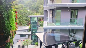 A modern building with a glass facade, a balcony, and a view of surrounding greenery.