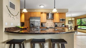 Une cuisine moderne dotée d’un îlot central, de meubles en bois, d’appareils électroménagers en acier inoxydable et d’une grande fenêtre qui laisse entrer la lumière naturelle.