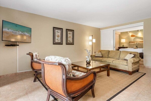 A living room with a sofa, armchairs, a coffee table, and a TV mounted on the wall.