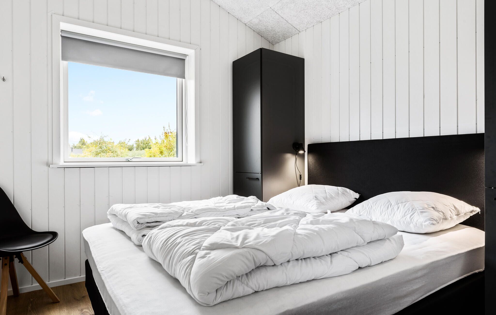 A bedroom with a bed, a window, a chair, and a wardrobe.