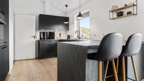 A modern kitchen with dark cabinets, a central island, and bar stools. - Pet friendly home in Sydals with WiFi (Sydals)