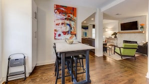 A modern kitchen with a dining area, a large abstract painting, and a TV mounted on the wall. - Safe, convenient Vacation Rental in Midtown - Sleeps 7 w/3 full bathrooms! (Atlanta)
