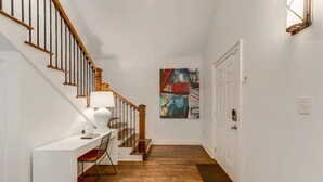 A hallway with a wooden staircase, a desk with a chair, and a colorful abstract painting on the wall. - Safe, convenient Vacation Rental in Midtown - Sleeps 7 w/3 full bathrooms! (Atlanta)
