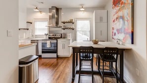 A modern kitchen with white cabinets, a stainless steel range hood, and a dining area with two black chairs. - Safe, convenient Vacation Rental in Midtown - Sleeps 7 w/3 full bathrooms! (Atlanta)