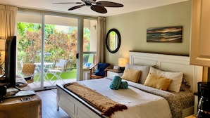 Une chambre d’hôtel avec un lit, un bureau, une chaise, un ventilateur de plafond, un tableau et une vue sur l’extérieur.