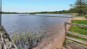 Ein ruhiger See mit einer Holzsteg, der ins Wasser hineinreicht, umgeben von Wiesen und Bäumen.