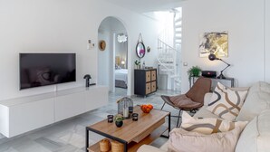 A modern living room with a flat-screen TV, a wooden coffee table, a sofa, and a staircase leading to a bedroom.