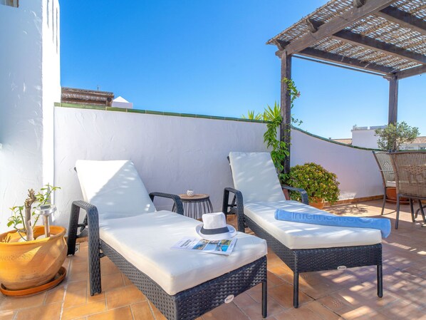A patio with two wicker lounge chairs, a small table, and a potted plant.