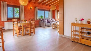 A spacious room with a wooden ceiling, a dining area with a table and chairs, a sofa, and a small side table with decorative items. - Cana Molí, ecohouse with sea views (Arta)