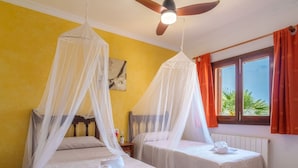 A room with two beds, each with a canopy, a ceiling fan, and a window with curtains. - Cana Molí, ecohouse with sea views (Arta)