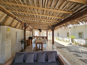 A covered outdoor seating area with a thatched roof, a dining table, and a sofa.