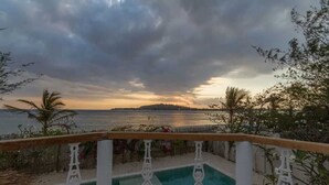 A pool with a wooden deck and a view of the sea and distant island. - VILLA AURORA (Gili Meno)