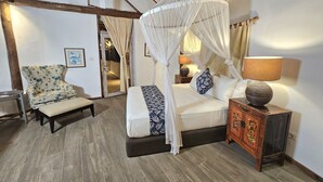 A bedroom with a four-poster bed, a chair, a nightstand with a lamp, and a wooden cabinet. - VILLA AURORA (Gili Meno)