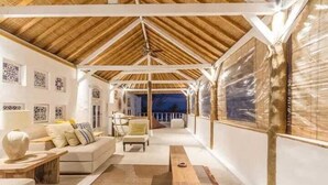 A spacious room with a high ceiling, wooden beams, a sofa set, and a view of the sea. - VILLA AURORA (Gili Meno)