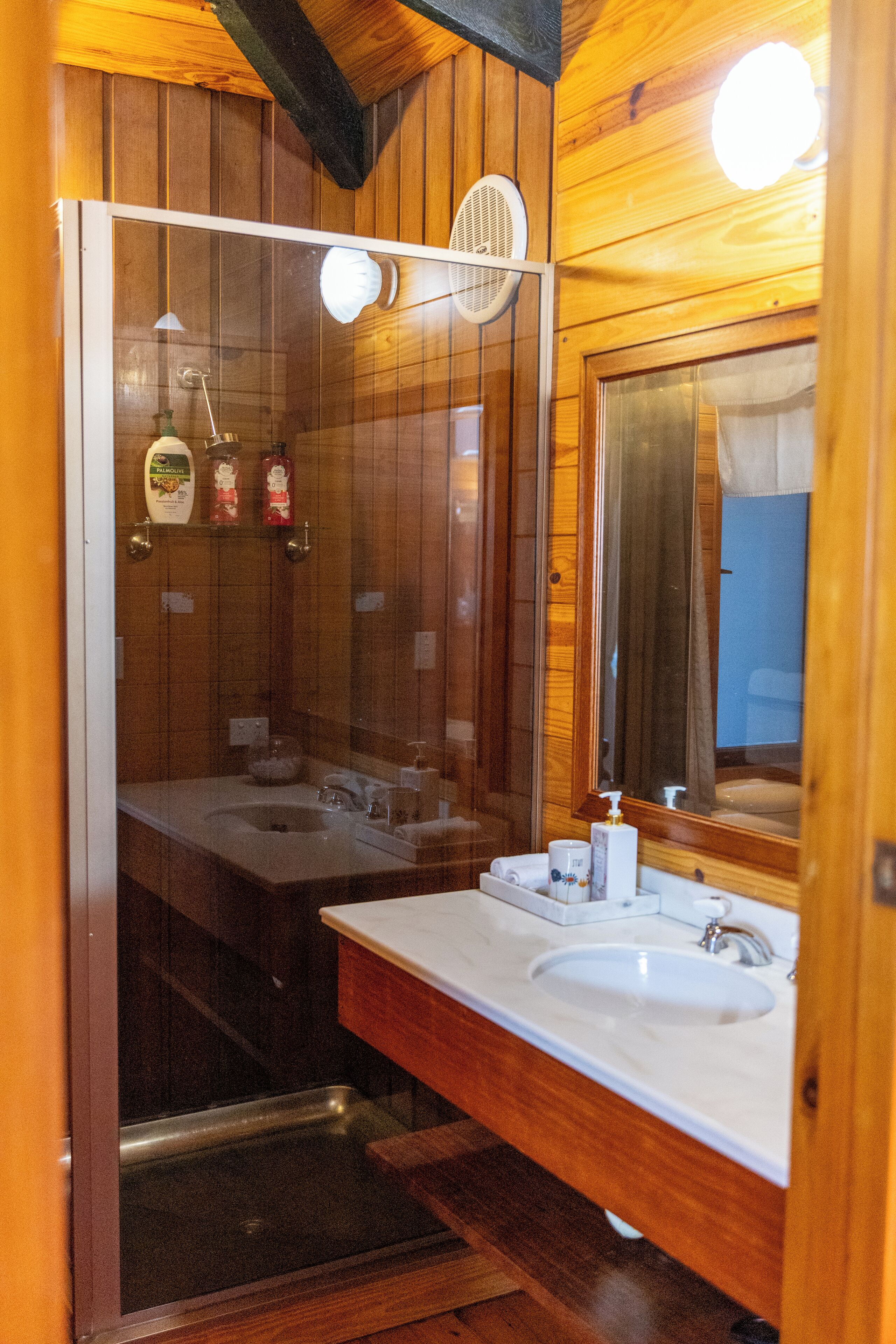 Bagno di una baita in legno con due lavandini, una doccia e uno specchio grande.