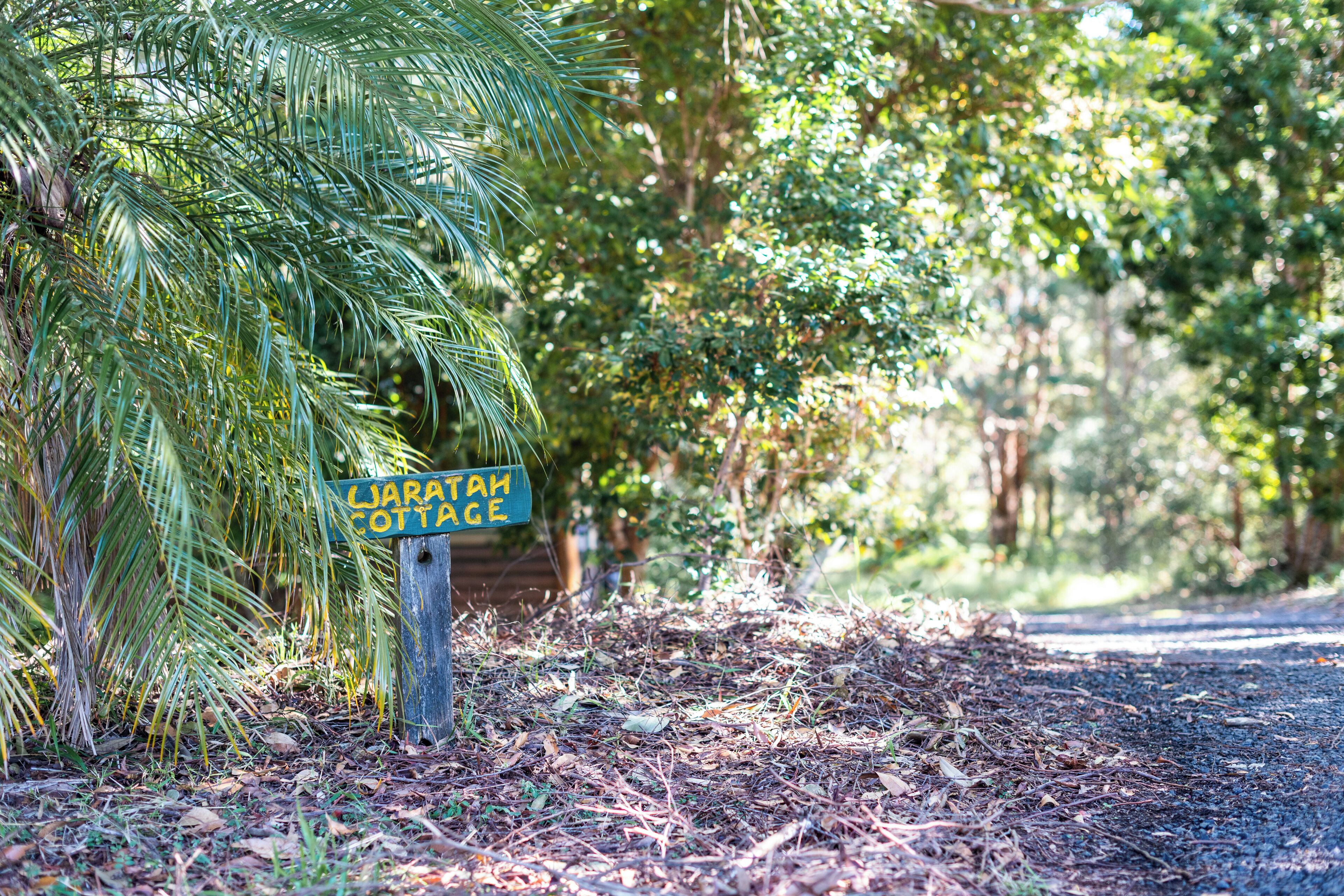 Señal para 'Jaratah Cottage' en una zona boscosa con un camino de grava.
