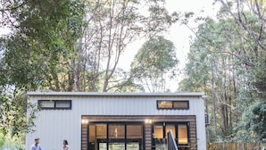 A modern building with a wooden deck, a glass door entrance, and a pathway leading to it. -  Kanimbia Cottages (Coolabine)