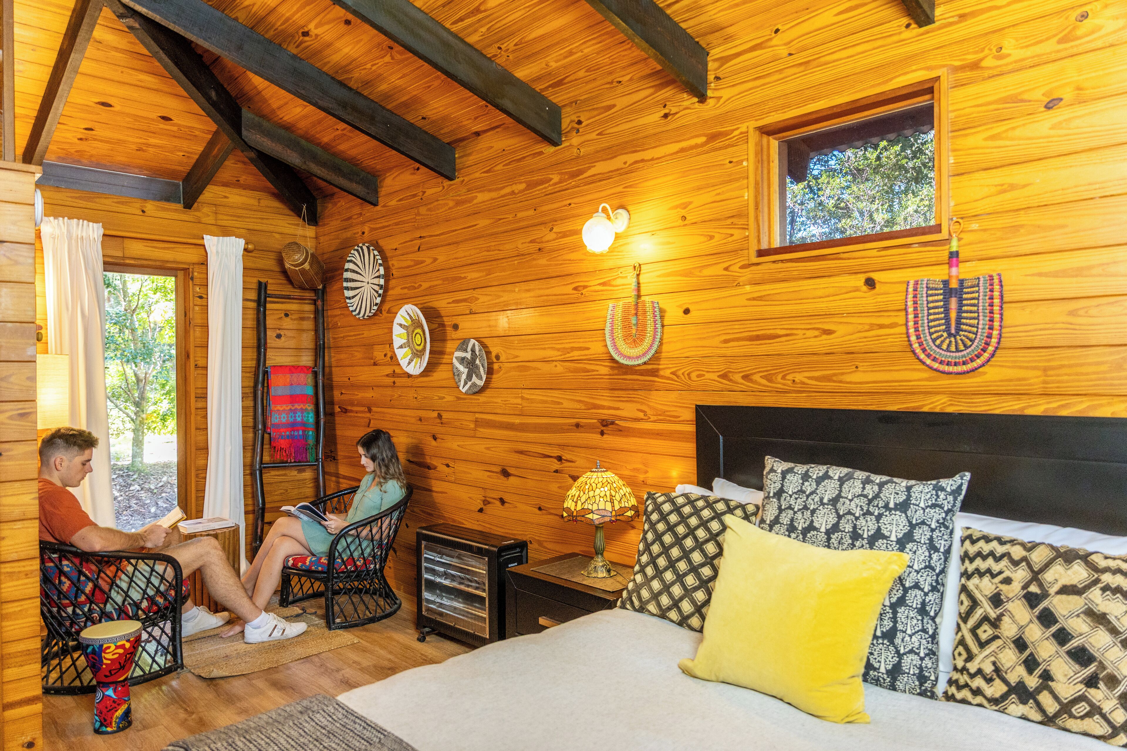 Una cabaña de madera acogedora con cama, dos sillas, una mesa y un pequeño calentador.