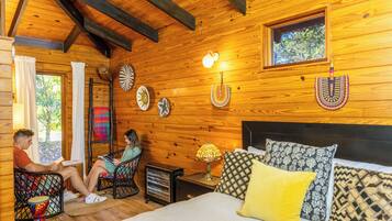 Una cabaña de madera acogedora con cama, dos sillas, una mesa y un pequeño calentador.