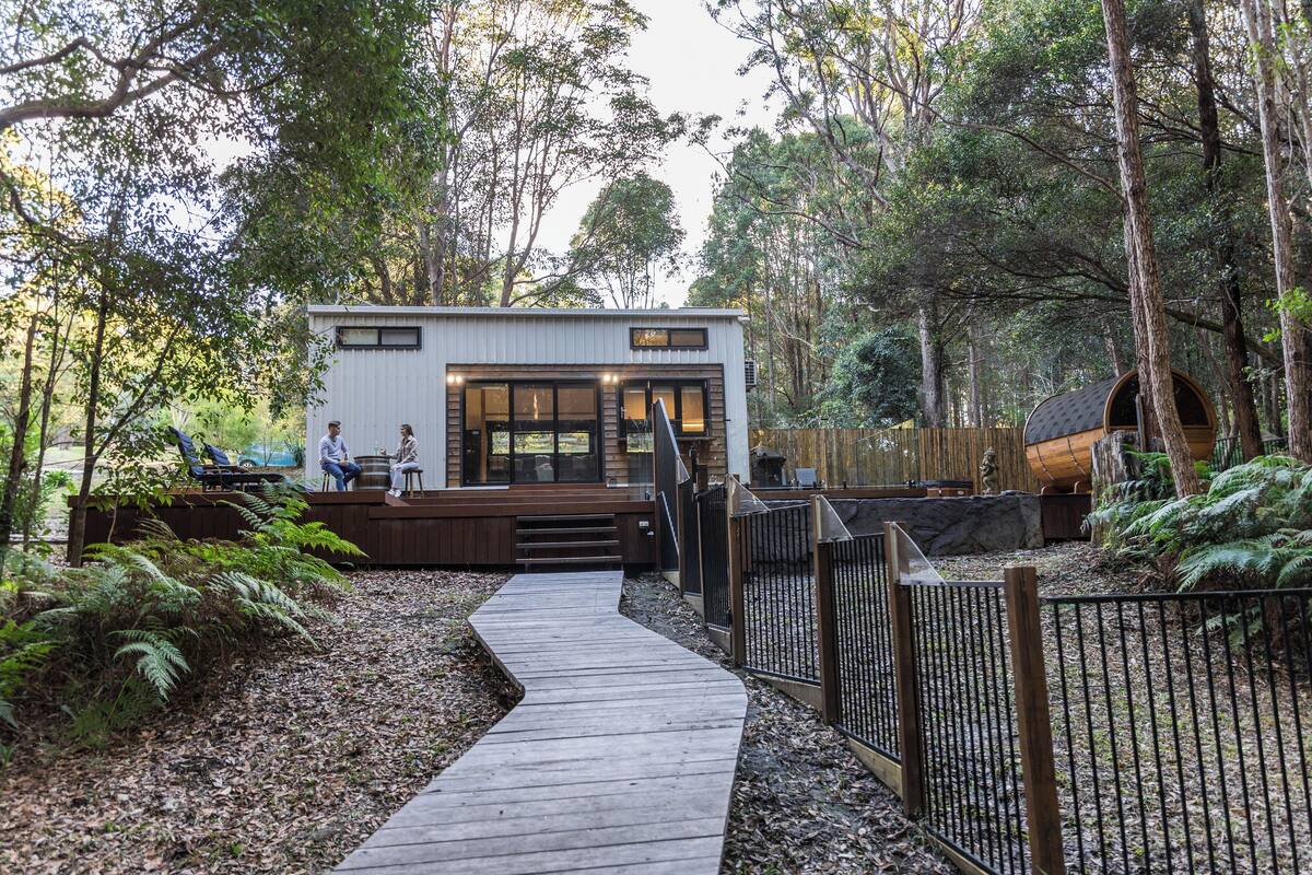 Una cabaña con terraza de madera, rodeada de un bosque frondoso.