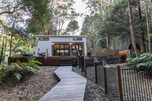 Una cabaña con terraza de madera, rodeada de un bosque frondoso.