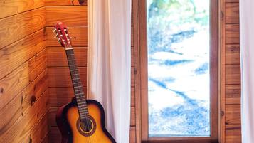 Ein Zimmer mit Holzwänden, einer Gitarre, die an der Wand lehnt, einem Fenster mit Vorhängen und einem Stapel Bücher auf einem Kissen.