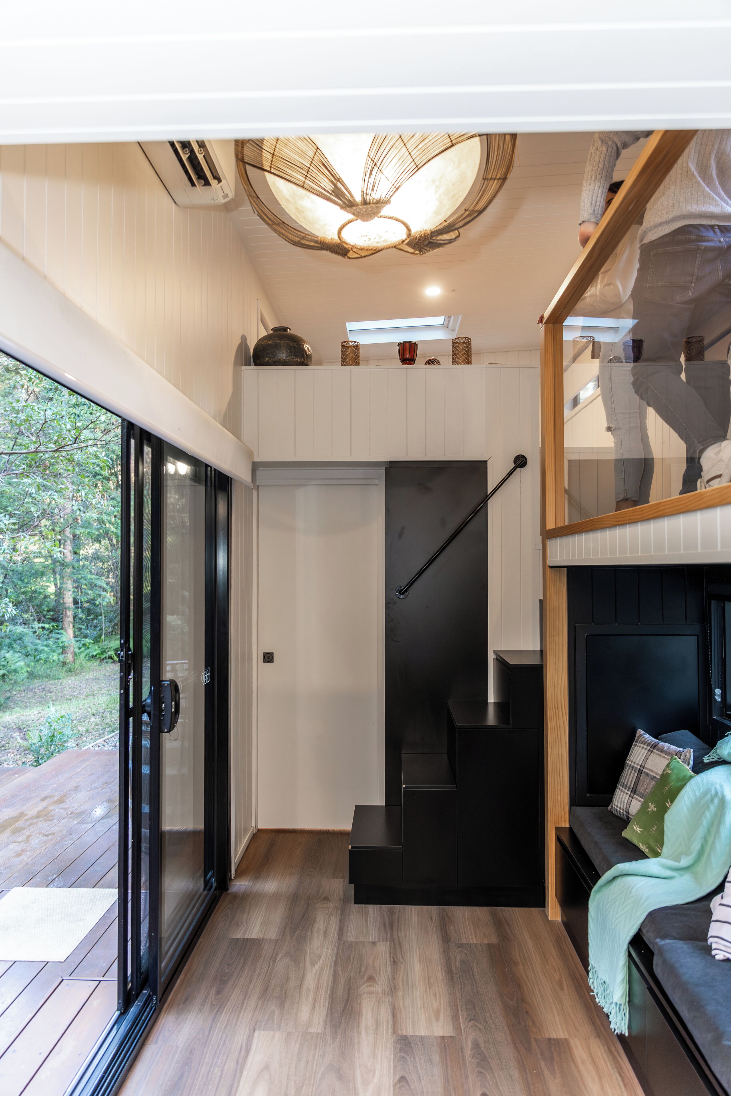 A modern interior with a staircase leading to a loft area, a glass door entrance, and a wooden deck outside.